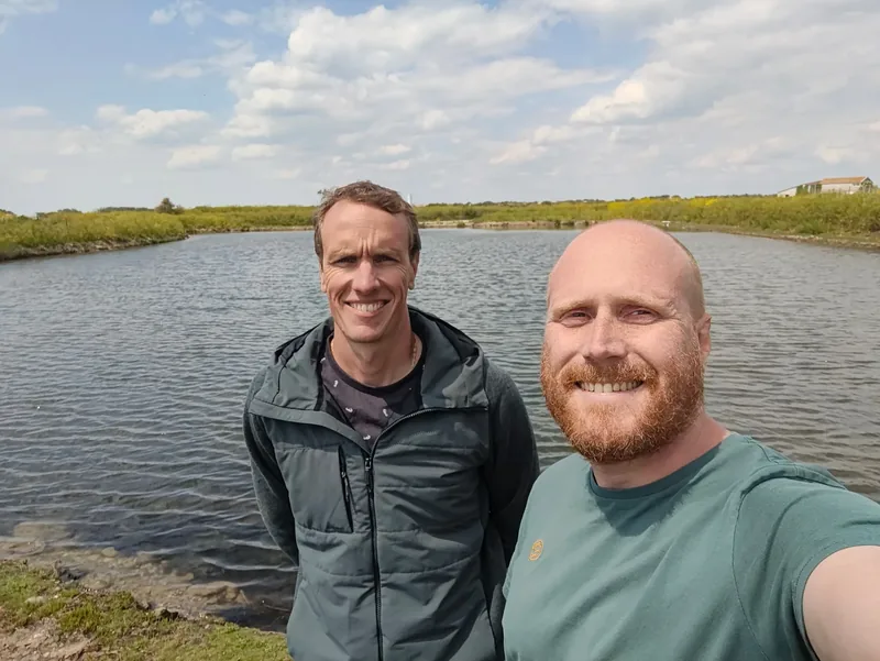 Two men standing beside a pond.
