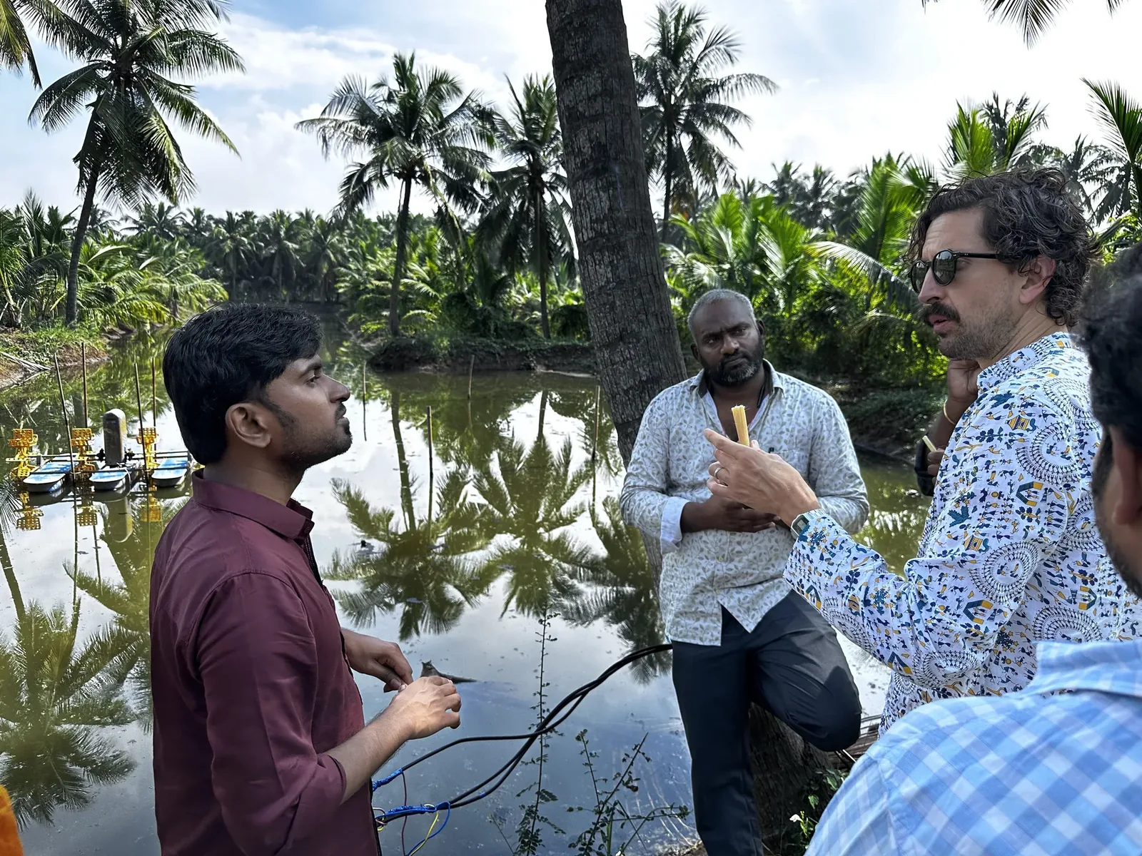 A group of men having a discussion close to a shrimp pond.
