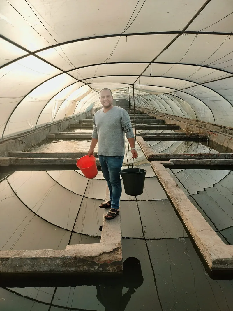 A man standing in a fish farm within a polytunnel.