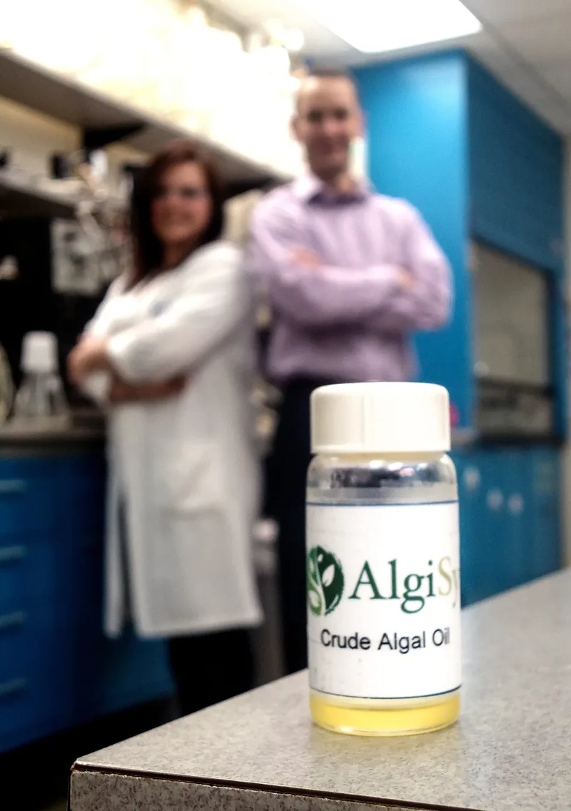A bottle of oil, with two people in the background.