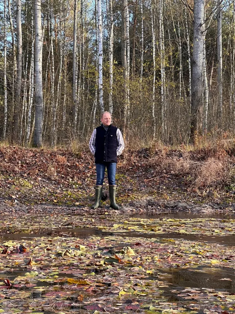 A man standing in front of a wood.